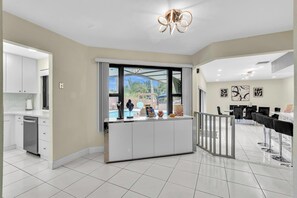 A modern kitchen with white cabinets, a built-in dishwasher, and a large window overlooking a pool area. - Beautiful Luxury Waterfront Heated Pool Home in Fort Lauderdale (Fort Lauderdale)