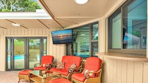Un espace extérieur aménagé, abrité et doté de meubles en osier et de coussins rouges, avec vue sur une piscine.