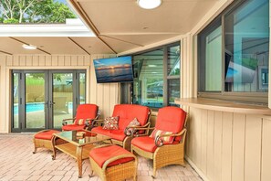 A covered outdoor seating area with wicker furniture and red cushions, overlooking a swimming pool. - Beautiful Luxury Waterfront Heated Pool Home in Fort Lauderdale (Fort Lauderdale)