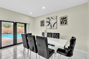 A dining area with a white table and black upholstered chairs, a large abstract painting, and a view of a swimming pool through glass doors. - Beautiful Luxury Waterfront Heated Pool Home in Fort Lauderdale (Fort Lauderdale)