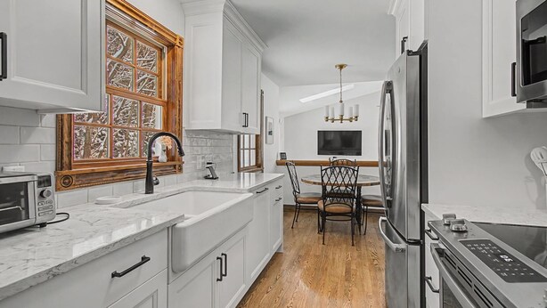 Una cocina moderna con armarios blancos, horno empotrado, microondas y una zona de comedor con mesa y sillas de madera.