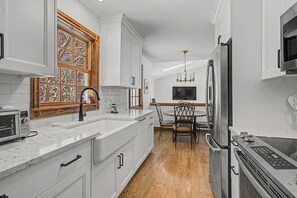 Una cocina moderna con armarios blancos, horno empotrado, microondas y una zona de comedor con mesa y sillas de madera.