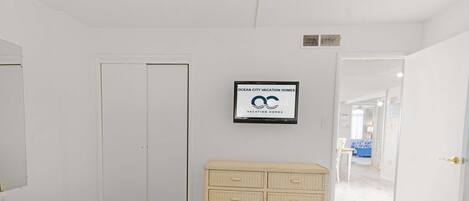 A bedroom with two beds, a white wardrobe, a framed sign, and a view into another room.