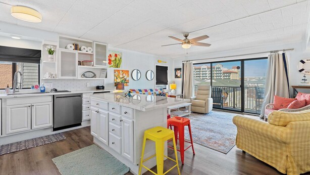 Cocina moderna con armarios blancos, una isla central y una zona de comedor con sofá amarillo y taburete rojo.