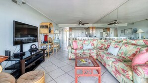 A living room with a flat-screen TV, a sofa, a coffee table, and a dining area with chairs. - Plaza 109 (Ocean City)