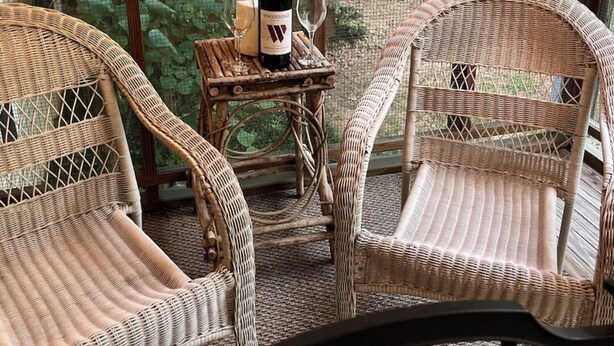 A room with two wicker chairs, a small table with a bottle and candle, and a view of greenery through large windows. - Tigers Den - Charming 4bd Lake Hartwell Lakefront house 11 miles to Clemson (Seneca)