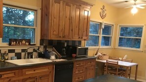 A kitchen with wooden cabinets, a black countertop, a microwave, and a dining area with a table and chairs. - Tigers Den - Charming 4bd Lake Hartwell Lakefront house 11 miles to Clemson (Seneca)