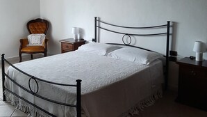 Une chambre à coucher comprenant un lit, une chaise, une table de chevet et une œuvre d’art accrochée au mur.