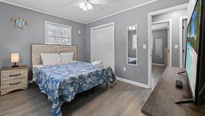 A bedroom with a bed, a nightstand, a ceiling fan, a TV, and a door leading to another room.