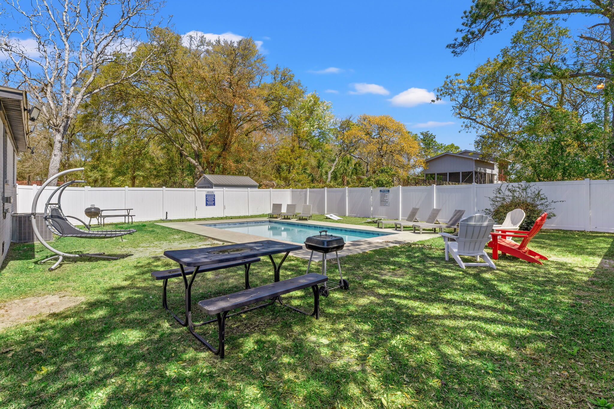 A backyard with a swimming pool, picnic tables, lounge chairs, and a barbecue grill.