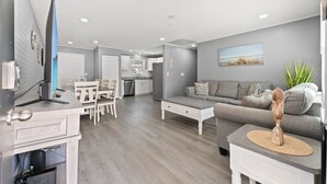 A modern living room with a grey sofa, a coffee table, and a dining area with a white table and chairs.