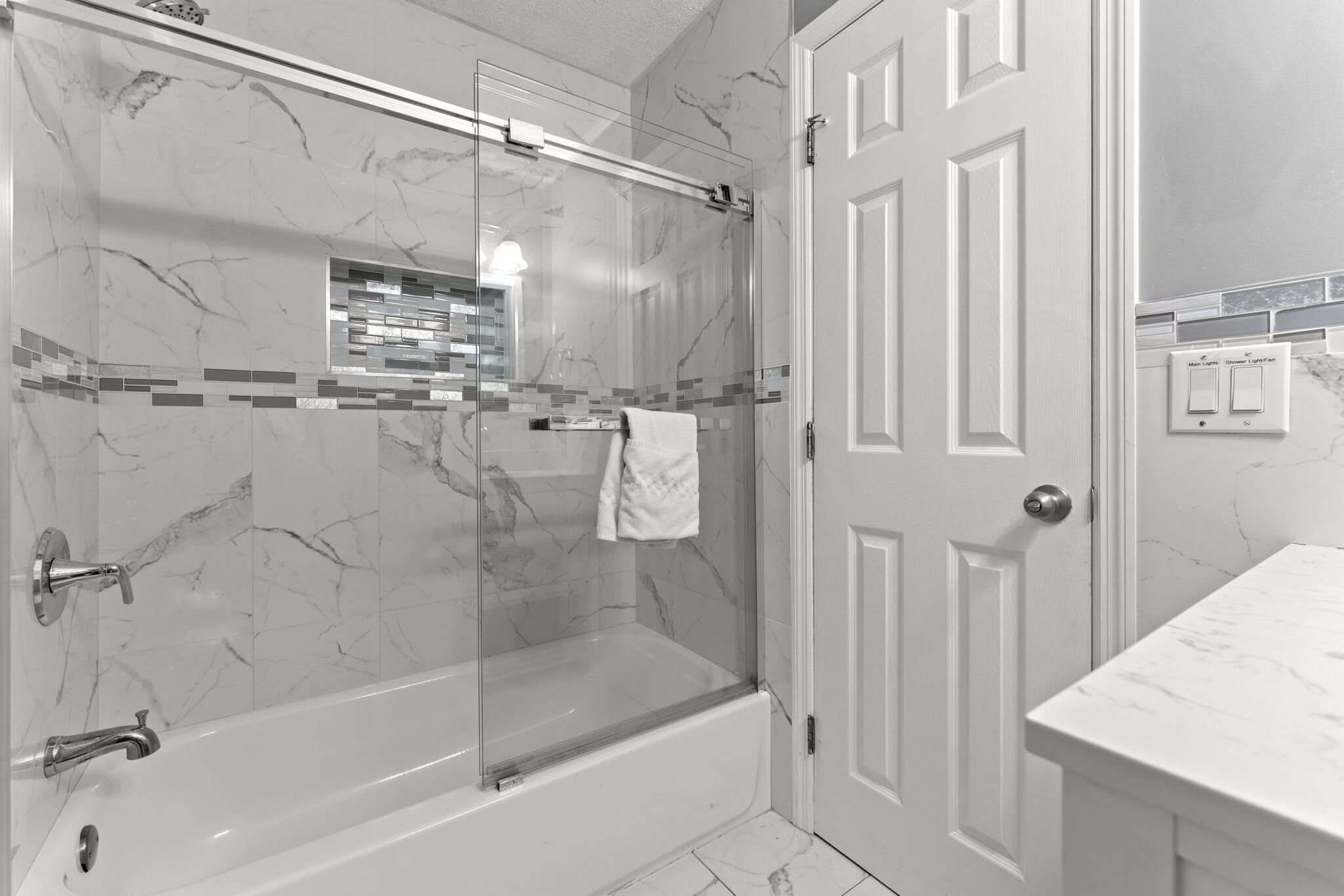 A bathroom with a glass-enclosed shower, a white bathtub, and a marble-tiled wall.