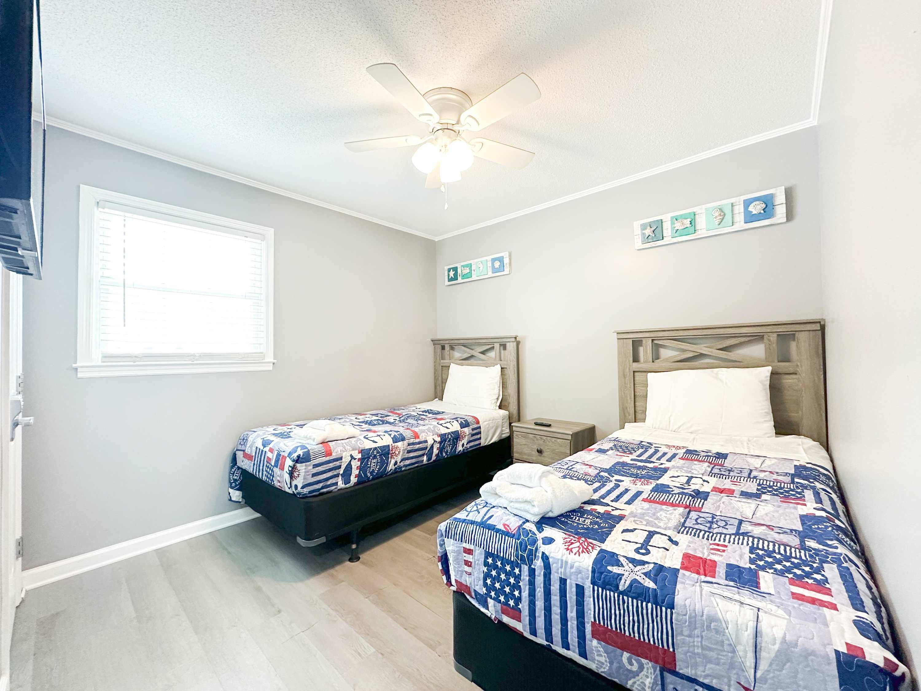 Une chambre avec deux lits, un ventilateur de plafond, une fenêtre et des décorations murales.