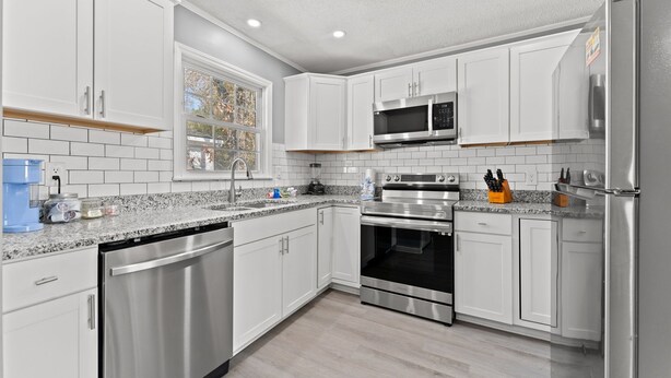 A modern kitchen with white cabinets, stainless steel appliances, and a window providing natural light.