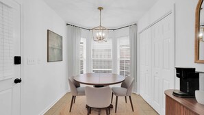 A dining area with a round table, four chairs, a chandelier, and a coffee maker on a wooden cabinet. - Modern Home Near EastChase & Maxwell AFB (Montgomery)