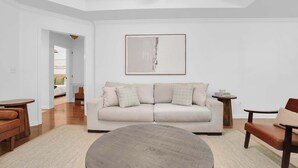 A modern living room with a beige sofa, a round coffee table, and a minimalist abstract painting on the wall. - Modern Home Near EastChase & Maxwell AFB (Montgomery)