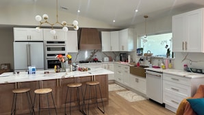 Una cocina moderna con armarios blancos, una isla grande con taburetes, electrodomésticos de acero inoxidable y una lámpara colgante.