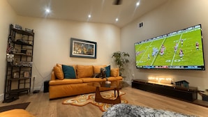 Sala de estar con un televisor de pantalla plana grande montado en la pared, un sofá de cuero, una mesa de centro y un tapete estampado.