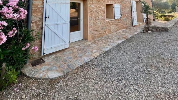 A stone building with a gravel driveway, white shutters, and a small garden with pink flowers. - LES CLAIRIANS - LE CANNET DES MAURES (LE CANNET DES MAURES)