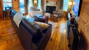 L’intérieur chaleureux d’un chalet avec un plafond en bois, une cheminée, un téléviseur et un canapé en cuir.