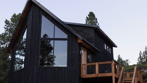 A modern wooden cabin with large windows, a wooden deck, and a staircase leading to a second level. - The Black Copper Cabin. Escape to a luxury mountain retreat. (Alton)