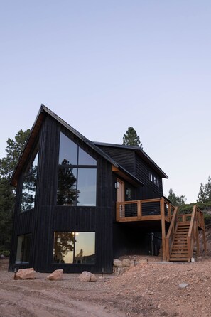 Ein modernes Holzhaus mit großen Fenstern, einer Holzdielen-Terrasse und einer Wendeltreppe zu einer zweiten Ebene.