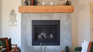 A modern living room with a fireplace, a wooden shelf with books and a deer head, and a decorative tree on the wall. - The Black Copper Cabin. Escape to a luxury mountain retreat. (Alton)