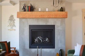 Ein modernes Wohnzimmer mit Kamin, einem Holzboden voller Bücher und einem Hirschkopf, sowie einem dekorativen Baum an der Wand.