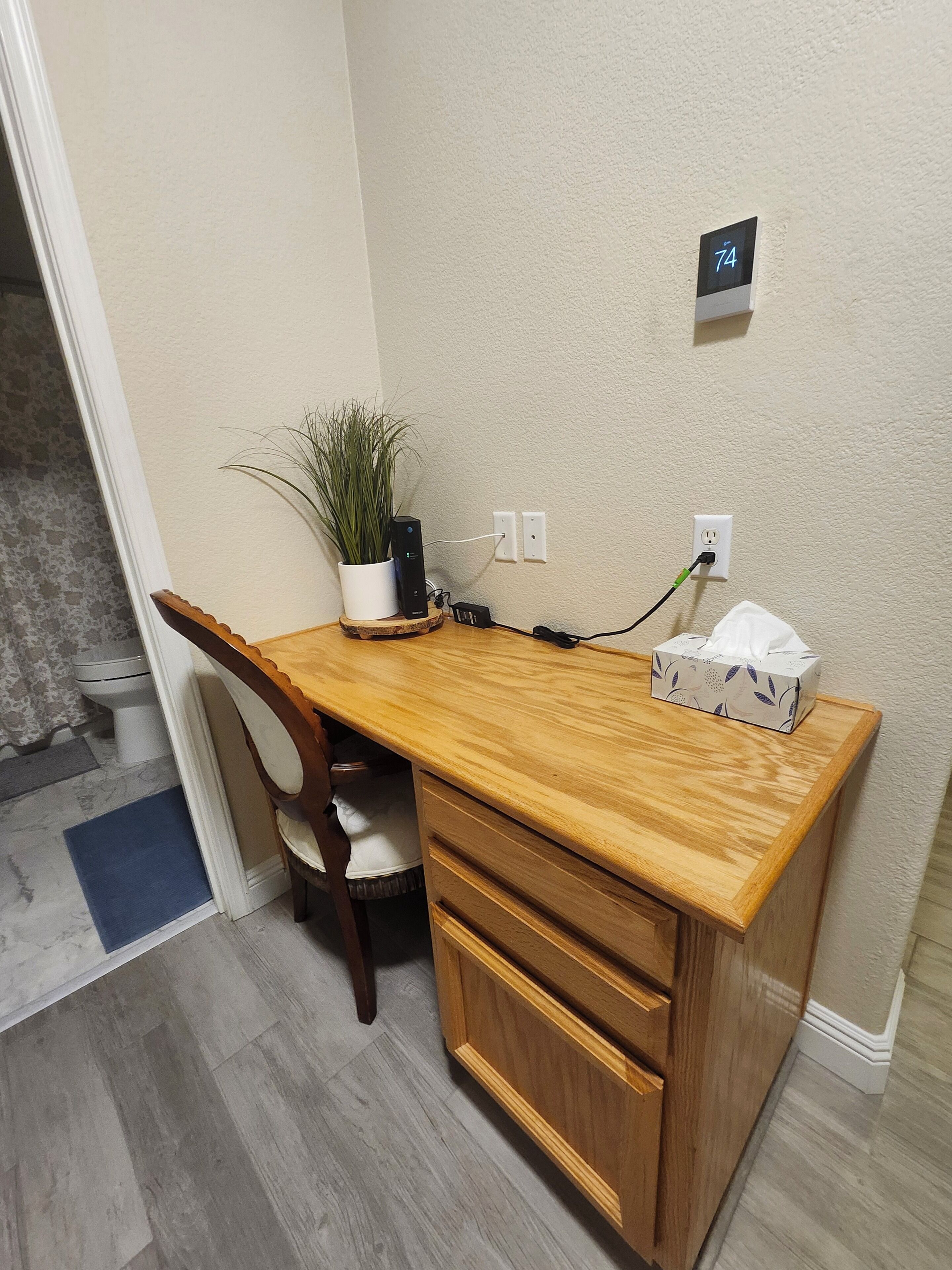 A wooden desk with a potted plant, a tissue box, and a power outlet on the wall.