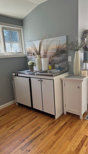 A kitchen with a built-in stove, a sink, and cabinets. There is a window with a view of trees and a painting on the wall.