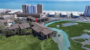 Un hotel frente al mar con varias construcciones, un estacionamiento y una masa de agua.