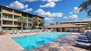Un hotel con piscina, sillas de descanso y un edificio de varios pisos con balcones.