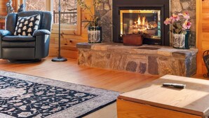 A cozy living room with a stone fireplace, wooden beams, a leather armchair, and a large window. - Shepardson Brookside: VAST+AT Hike | A/C | Brook (Stratton)