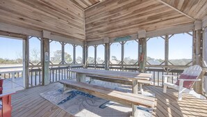 A covered outdoor deck with a picnic table and chairs, large windows, and a view of the landscape. - 1708 - Islander Gulls: Spacious 4BR house in Corolla, perfect for families! (Corolla)