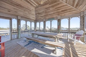 A covered outdoor deck with a picnic table and chairs, large windows, and a view of the landscape. - 1708 - Islander Gulls: Spacious 4BR house in Corolla, perfect for families! (Corolla)