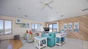 A living room with a sofa, a TV, a ceiling fan, and artwork on the walls. - 1708 - Islander Gulls: Spacious 4BR house in Corolla, perfect for families! (Corolla)