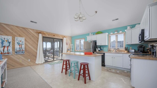 A modern kitchen with white cabinets, a central island with stools, and a view to the outside. - 1708 - Islander Gulls: Spacious 4BR house in Corolla, perfect for families! (Corolla)