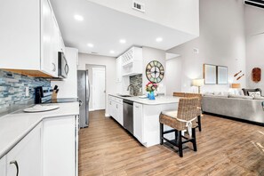 Una cocina moderna con armarios blancos, una isla central y un comedor con sillas de mimbre.
