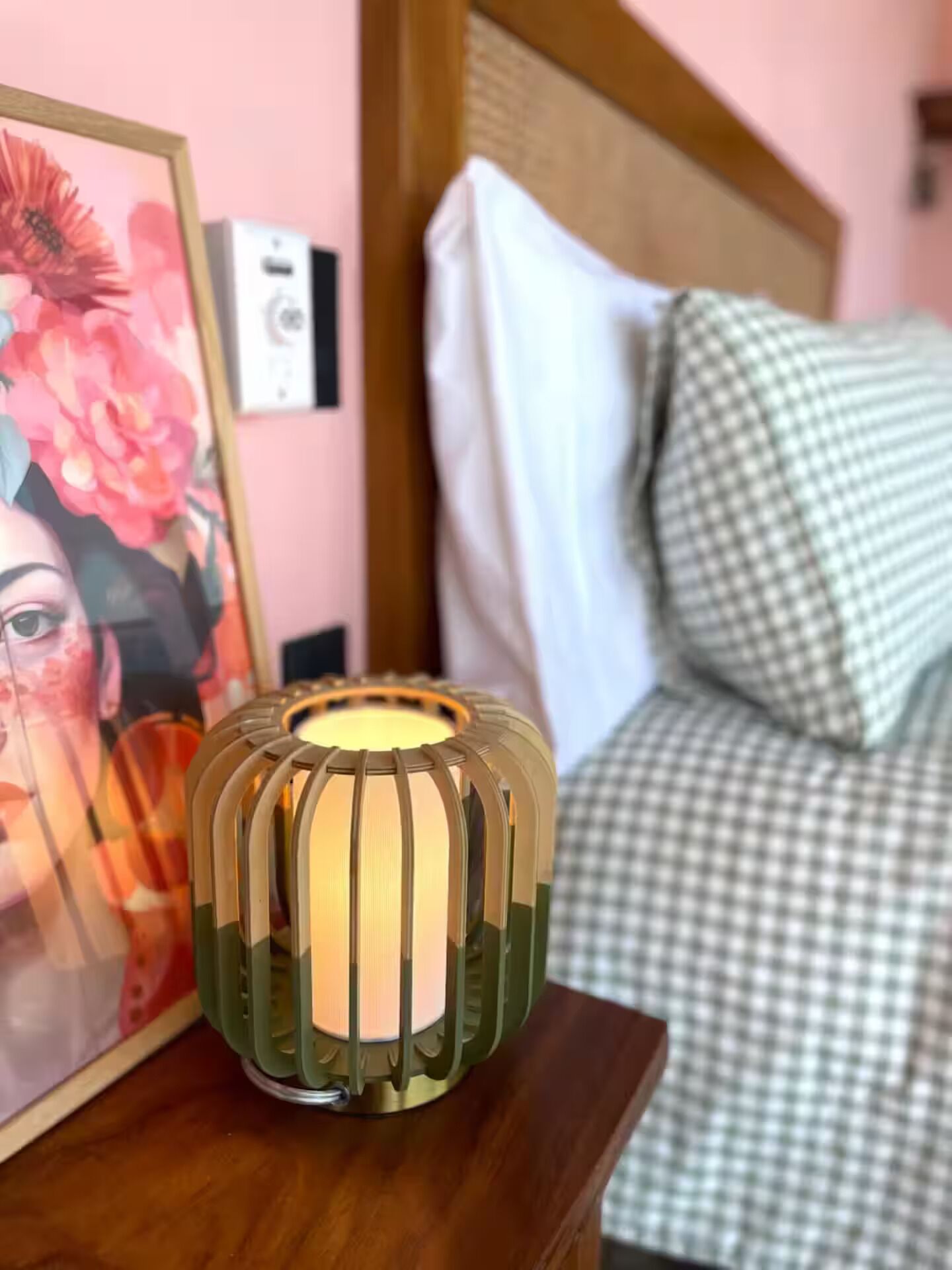 A bedside table with a decorative lamp, a framed floral artwork, and a checkered bedspread.