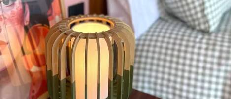 A bedside table with a decorative lamp, a framed floral artwork, and a checkered bedspread.