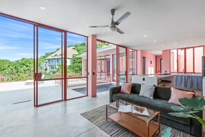 A spacious living area with a large sliding glass door leading to an outdoor terrace, a ceiling fan, and a modern sofa with cushions. - Casa Trifecta! Ocean views, Private pool and a 5min walk to the beach! (Sayulita)
