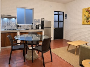 A compact kitchen with a gas stove, a coffee maker, and a refrigerator. There is a dining area with a round glass table and four chairs. - 5 de Diciembre 1BR 4 Blocks to Camarones Beach (Puerto Vallarta)