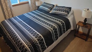 Uma cama com colcha estampada e almofadas, um abajur e um quadro na parede.