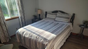 Cama bem arrumada com roupa de cama listrada, mesa de cabeceira com abajur e uma pequena planta em vaso.