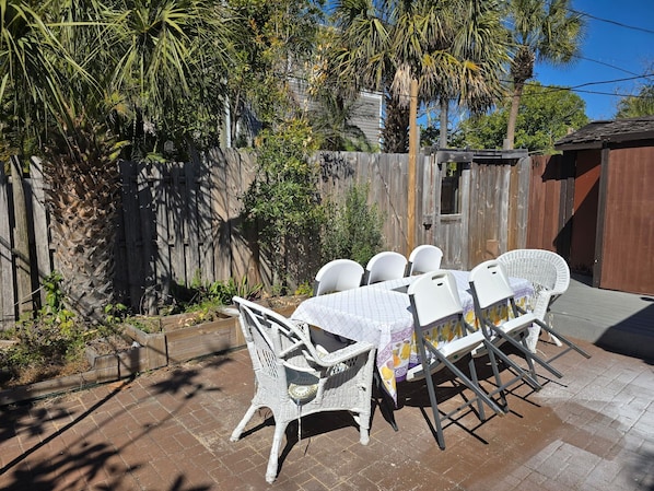 A patio with a table and chairs, surrounded by a wooden fence and palm trees.