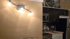 Une cuisine compacte avec une table ronde en verre, deux chaises, un four à micro-ondes, un réfrigérateur et un luminaire fixé au mur.