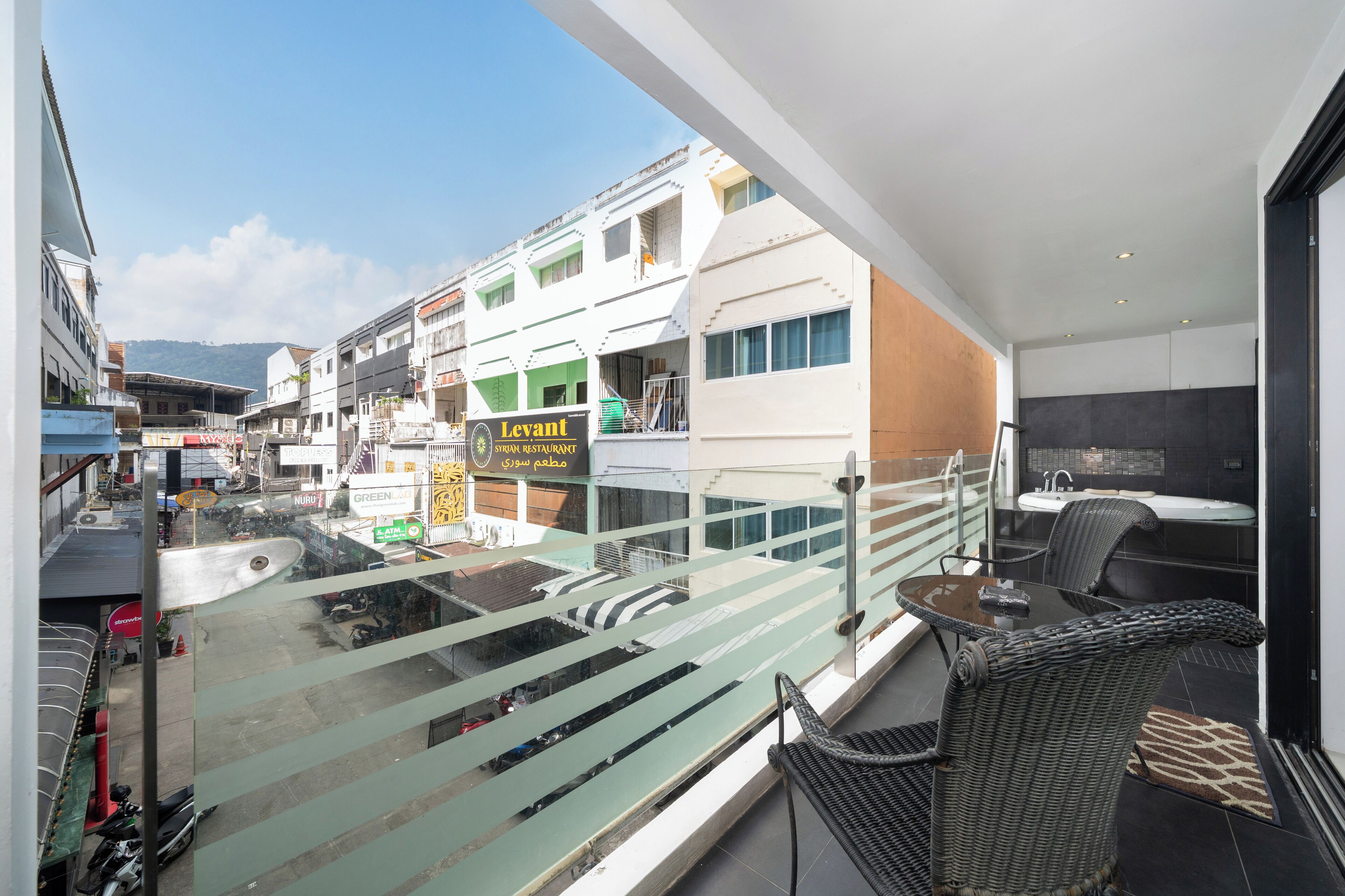 Ein Balkon mit Glasgeländer, der auf eine Straße mit Geschäften und einem Restaurant namens "Levant" blickt.