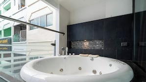 Ein modernes Badezimmer mit einer großzügigen, freistehenden Badewanne, einem gläsernen Balkon und Blick auf die Stadt.