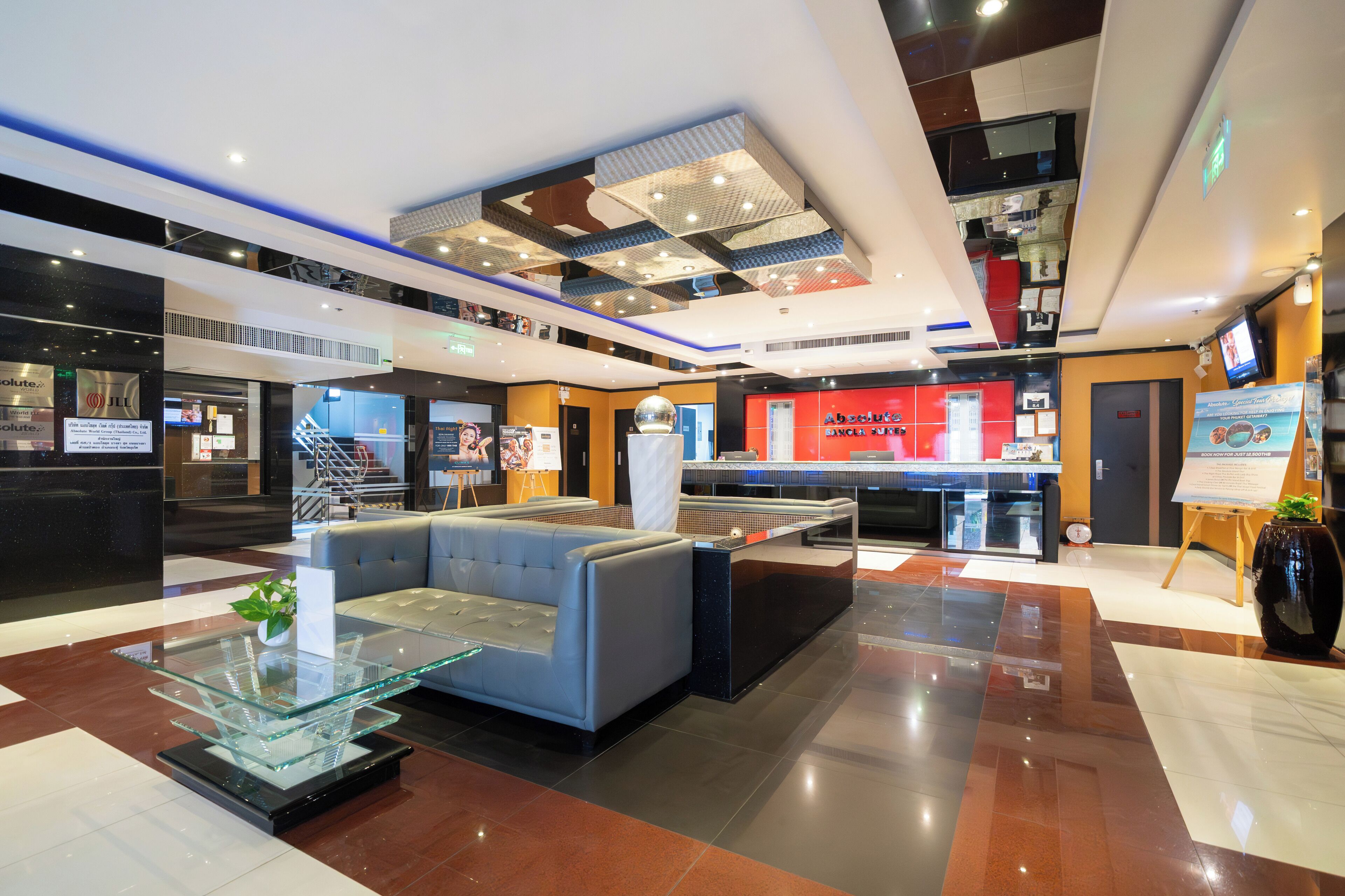 A modern lobby with a glass coffee table, a seating area, a reception desk, and a staircase.