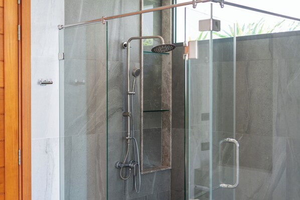 Une douche moderne, entièrement vitrée, dotée d’un pommeau de douche à main et d’un flexible de douche à main.